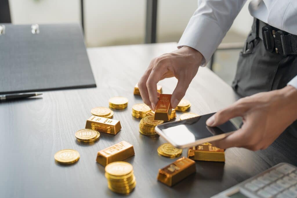 Un investitore analizza lingotti e monete d'oro sulla scrivania con uno smartphone, rappresentazione moderna di come investire in oro fisico